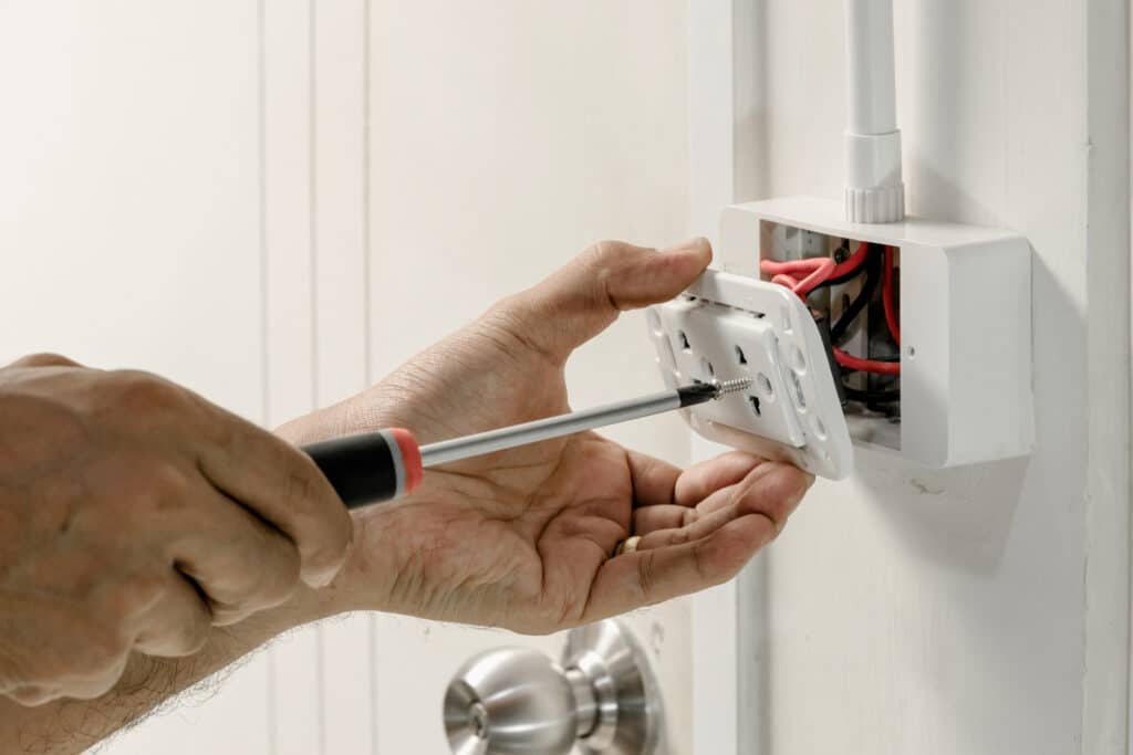 electrician using a screwdriver to attach the power cord to the wall outlet.
